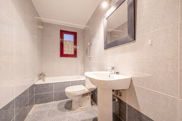 bathroom with bathtub, mirror with rectangular frame attached to the wall, two-tone tiles and white toilets