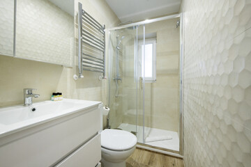 Bathroom with white furniture, mirror with sconces, tile panel, chrome towel rail and shower tray with sliding screens