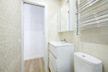 Fototapeta na wymiar Bathroom with white cabinet, mirror with sconces, tile panel, chrome towel rail and white wooden sliding door