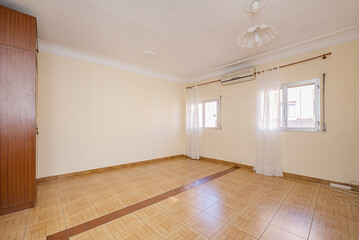 Empty room with stoneware floor, air conditioner between two aluminum windows with white curtains