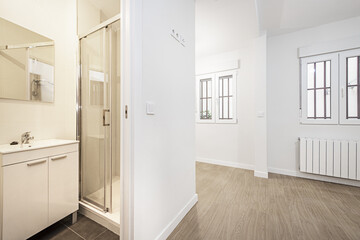 empty room with a pair of white aluminum windows with metal bars and access to a bathroom with white furniture and a shower cabin