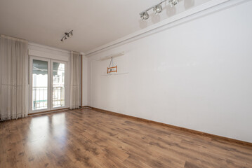 Empty room of a loft apartment with white painted walls, plaster moldings on the ceiling and exit to a terrace with aluminum and glass doors and white curtains
