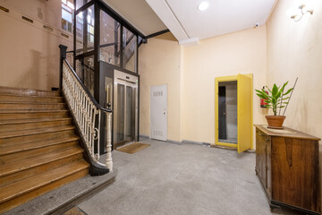 Renovated glass and metal elevator inside an old building with wooden steps staircase and metal balustrade