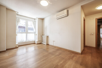 Living room of an empty house with radiator covers, air conditioning and white aluminum window with curtains