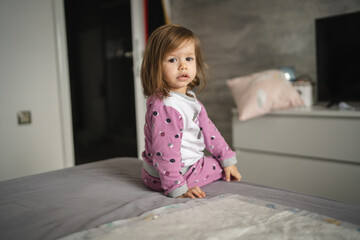 Fototapeta premium One girl small caucasian toddler sit on bed wear pajamas in morning