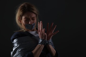 Scared woman taped up and taken hostage on dark background. Space for text