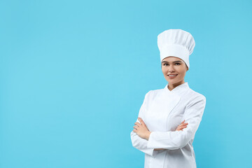 Happy female chef wearing uniform and cap on light blue background. Space for text