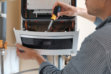 Man repairing gas boiler with screwdriver indoors, closeup