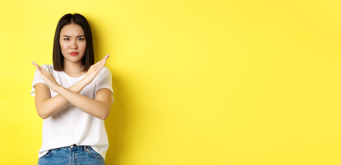 Serious and assertive korean woman showing cross stop gesture, frowning and telling no, prohibit...
