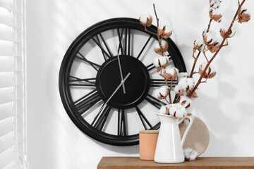 Cotton branches with fluffy flowers and home decor on wooden table near white wall. Space for text