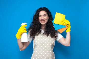 young girl cleaner in uniform holds a spray and rags on a blue background, a woman housekeeper in...