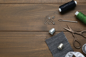 Flat lay composition with thimbles and different sewing tools on wooden table. Space for text