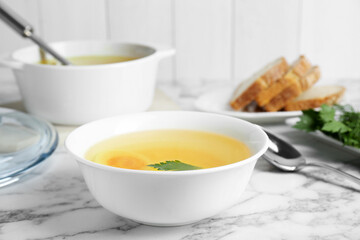 Delicious bouillon with egg and parsley in bowl on white marble table