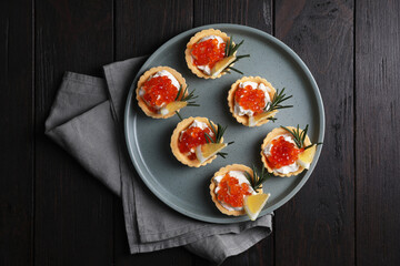 Delicious tartlets with red caviar and cream cheese served on wooden table, top view
