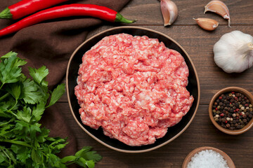 Bowl of raw fresh minced meat and ingredients on wooden table, f