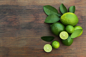 Whole and cut fresh ripe limes with green leaves on wooden table, flat lay. Space for text