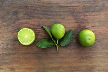 Whole and cut fresh ripe limes with green leaf on wooden table, flat lay