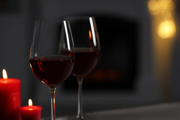 Glasses of red wine and burning candles against blurred background, space for text. Romantic atmosphere
