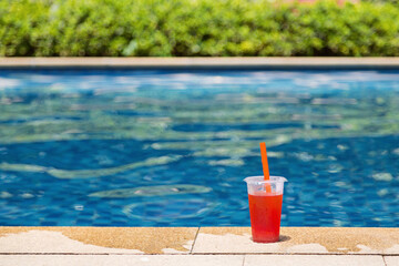 Fototapeta na wymiar Fresh glass of watermelon smoothie drink standing on border of swimming pool. holiday tropical concept. Mockup with copy space