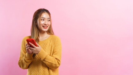 Young women holding smartphone and looking outside with empty space on isolated pink background