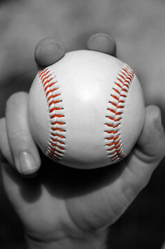 Selective color black and white image of a hand pitching a baseball. Retro nostalgic.