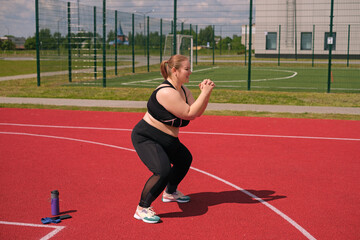 A happy cheerful overweight plump young woman does a squat exercise with her hands in front of her....