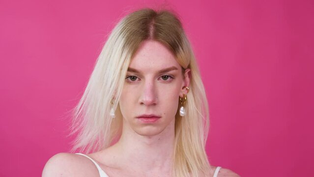 Young transgender man transsexual applying make-up on a pink background