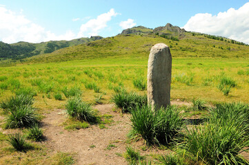 A triangular white granite monolith surrounded by low bushes in the center of a picturesque valley...
