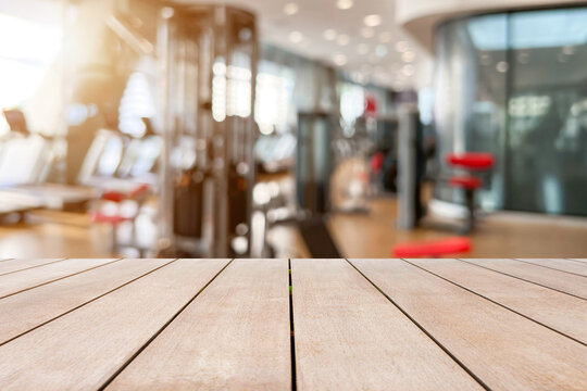 Empty old wooden table in front of blurred background of the gym equipment and machine weight training zone. Can be used for display or montage for show your products.