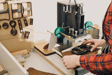 Molds for cutting leather. Cropped view of the woman hands holding leather and cutting it with special press machine. Tailoring and handicraft concept. Closeup