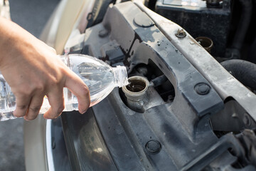 Hand holding water bottle is pouring water into the car radiator