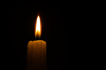 Single burning wax candle against a black background