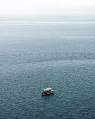 A small, forgotten boat sits idly on the calm surface of the vast and serene Ohrid lake, surrounded by breathtaking natural beauty.
