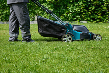 Picture of a man in overalls with a lawn mower, cutting green grass in a modern garden against a...