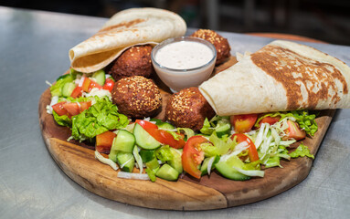 Delicious Falafel dish on a wooden plate close-up. tortilla, vegetable salad, and tahini sauce.