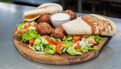 Delicious starter Falafel dish on a wooden plate in the Lebanese restaurant kitchen. flatbread, vegetable salad, and tahini sauce.