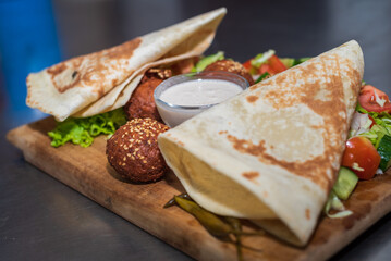 Presenting the middle eastern Lebanese dish Falafel on a wooden plate. tortilla, vegetable salad, and tahini sauce.