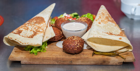 Presenting the middle eastern Lebanese dish Falafel on a wooden plate. tortilla, vegetable salad, and tahini sauce.