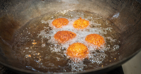 Deep frying falafel balls in wok, hot cooking oils bubbling and falafel balls turned golden brown color