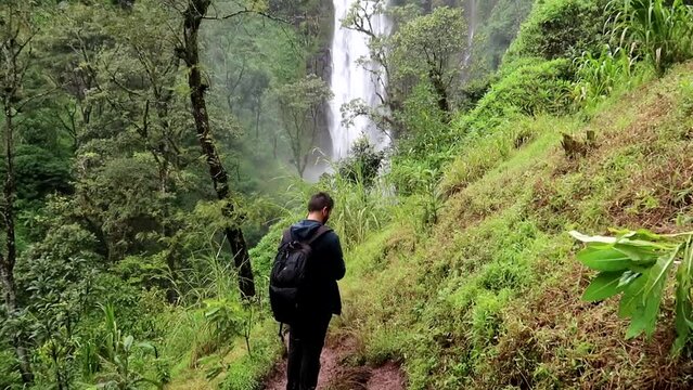 Young backpacker man checking the flight of a drone in Materuni Waterfall. Awesome tropical epic landscape to capture
