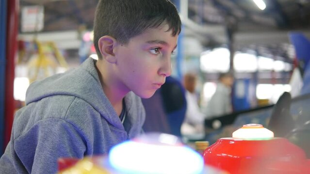 A boy concentrating hard while playing at the arcade.