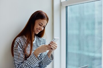 Woman holding a phone smile with teeth in the background of the window, the concept of working and education online via the Internet
