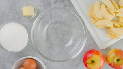 Apple cake recipe. Sliced apples on a cutting board, sugar, eggs, and butter, and a glass bowl close-up on a kitchen table