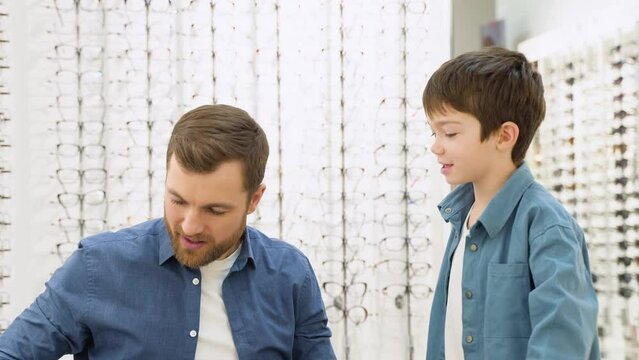 Family buy glasses. Father and son in a blue shirts choosing glasses