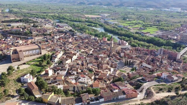 Aerial view of olt town of Fraga on bank of Cinca river in province of Huesca overlooking brownish tiled roofs of residential buildings and Church of San Pedro on sunny spring day, Spain
