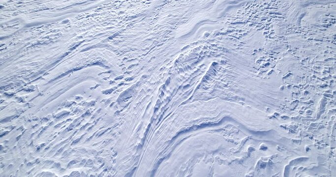 The surface of a snow-covered field with small dunes. Snow dunes created by the wind, aerial shot. Snow covered field. Snow covered texture pattern. Arctic climate. Winter season