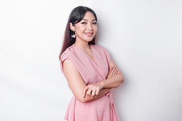 Obraz premium Portrait of a confident smiling Asian woman dressed in pink, standing with arms folded and looking at the camera isolated over white background
