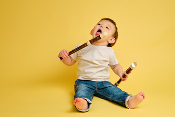 Toddler baby with a flute wind musical instrument on a studio yellow background. A happy child...