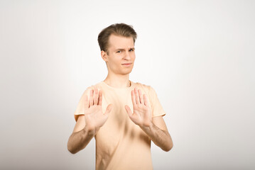 The guy avoids the suggested risks, shakes his hands in stop and frowns on a white background.