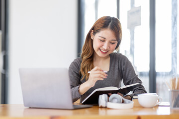 Distance Education. Portrait of smiling Asian woman sitting at desk, using laptop and notebook, taking notes, watching tutorial, lecture or webinar, studying online student learning remotely.